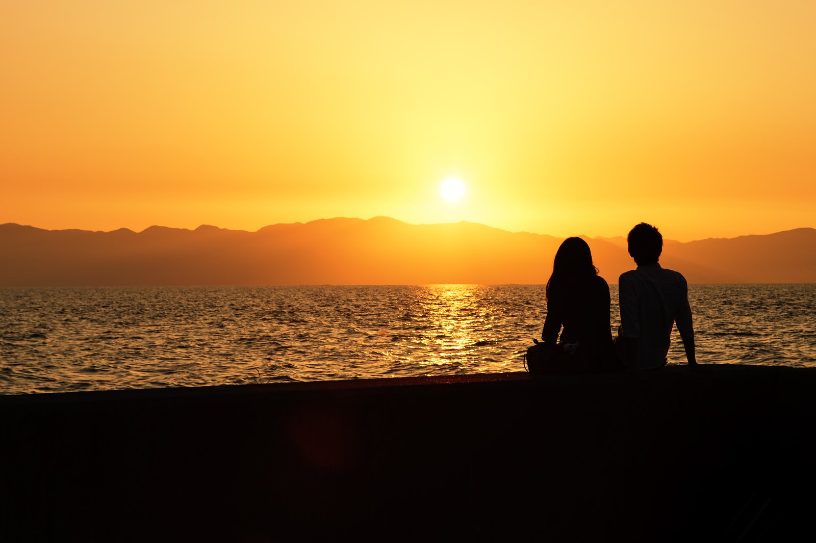 夕焼けの海辺に座る二人のシルエットの写真素材 - フリー素材ぱくたそ