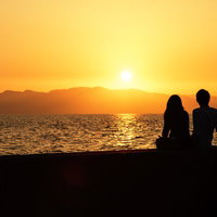 夕焼けの海辺に座る二人のシルエットの写真