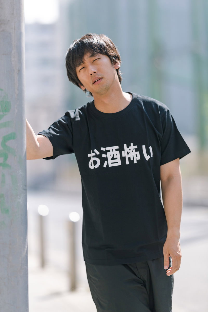 二日酔いで頭に手を当てて辛そうな表情を浮かべる黒いTシャツの男性［モデル：大川竜弥］