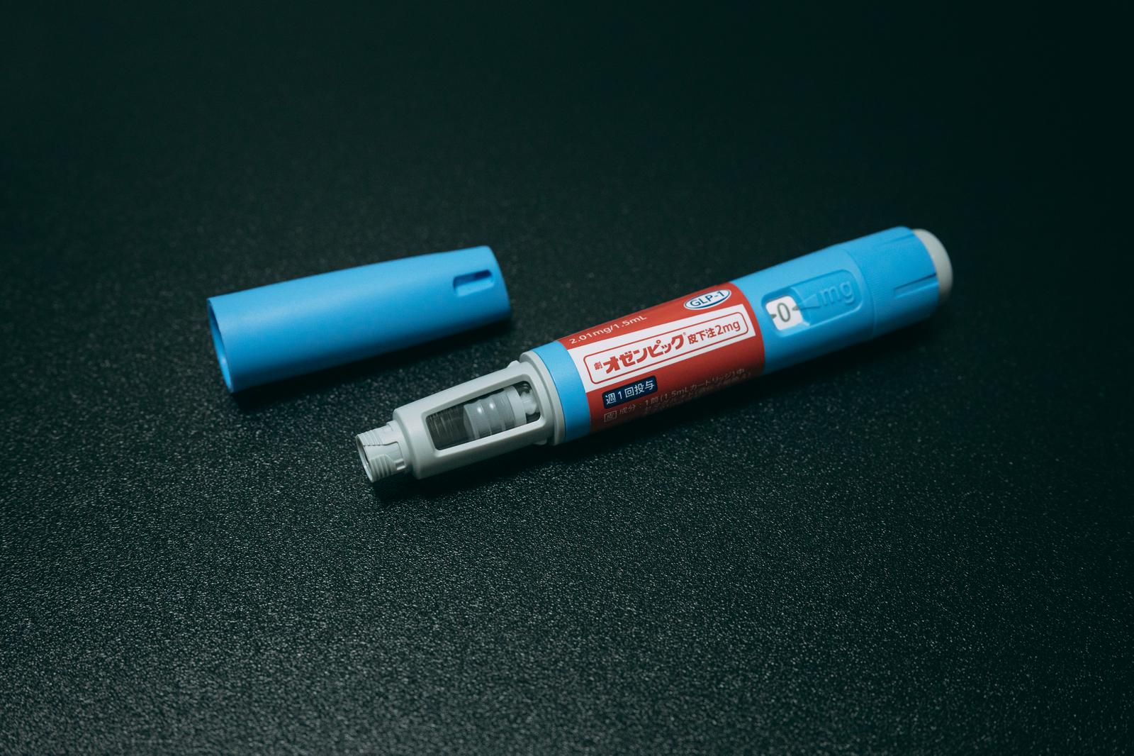オゼンピック皮下注の注射ペンと青いキャップが深緑色の背景に置かれている