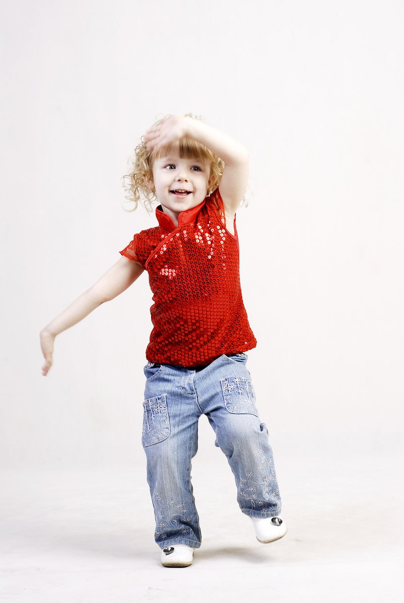 白い背景で赤いシャツを着て元気よく手を振る金髪の女の子［モデル：モデルファクトリー］