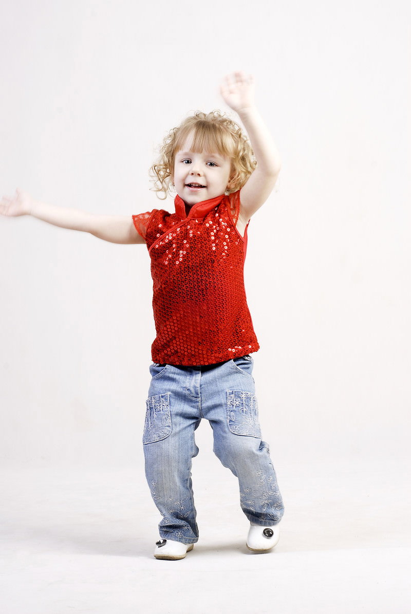 赤いトップスにデニムを着た金髪の外国の女の子が両手を広げてポーズ［モデル：モデルファクトリー］