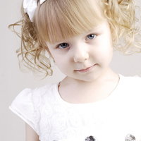 パーティ用におめかしした、ブロンドヘアのカール髪の幼い女の子の写真