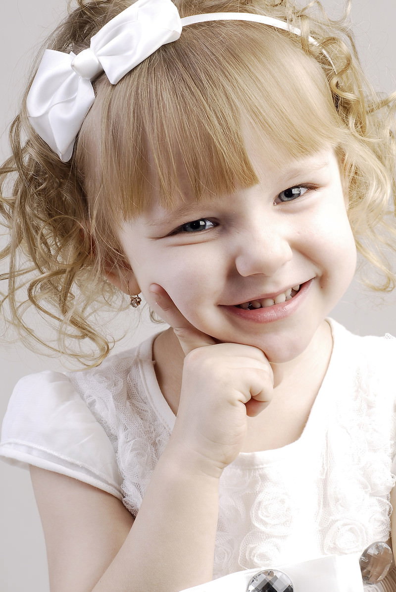 白いヘアアクセサリーを付けたブロンドヘアの女の子がひきつった笑顔を見せている［モデル：モデルファクトリー］