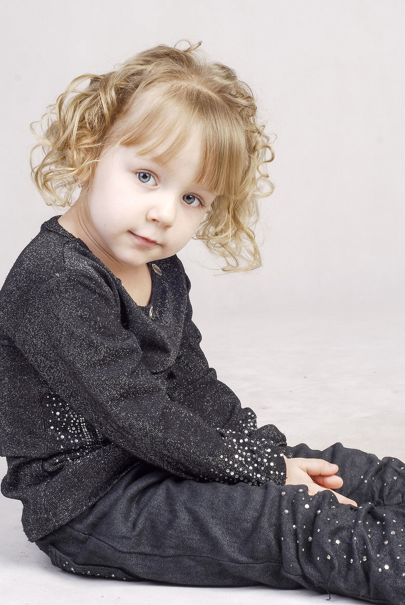 ブロンドヘアの女の子が座って上を見上げている様子［モデル：モデルファクトリー］