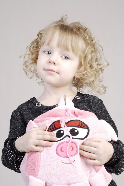 おどけた表情でぶたのバッグを持つ幼い女の子