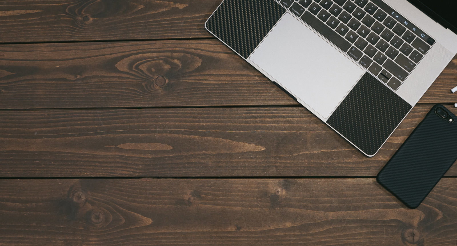 木目テーブルの右上にノートパソコンとスマートフォンが置いてある