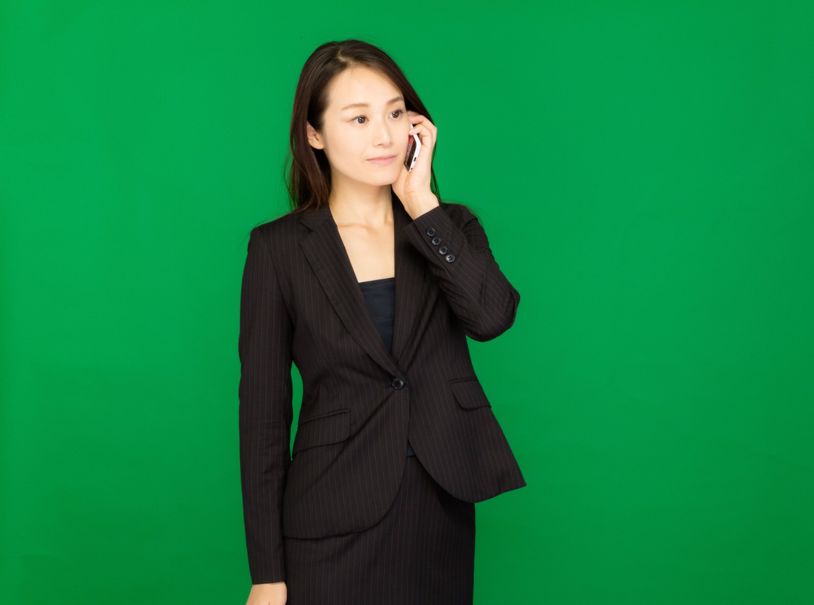 グリーンバックの前でスマートフォンで通話するスーツ姿の女性［モデル：土本寛子］