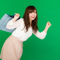 ショッピングバッグを肩に担いで走るショッピングに夢中な女性（グリーンバック）の写真