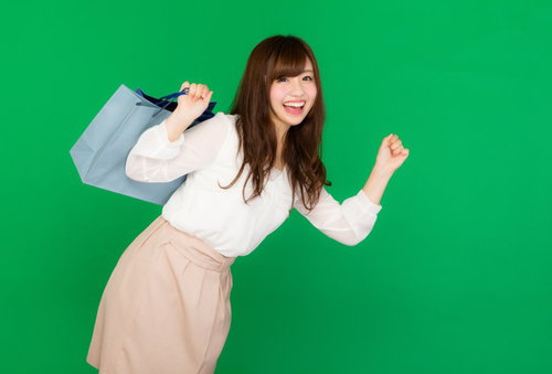 ショッピングバッグを肩に担いで走るショッピングに夢中な女性（グリーンバック）