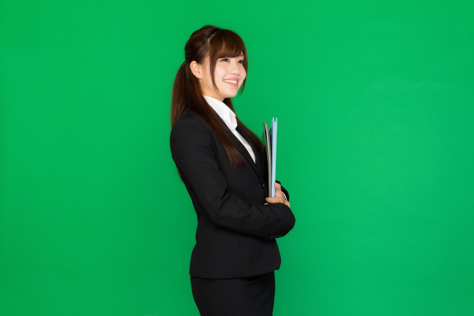 グリーンバックの前でリクスー姿で書類を持つ就活女性［モデル：河村友歌］