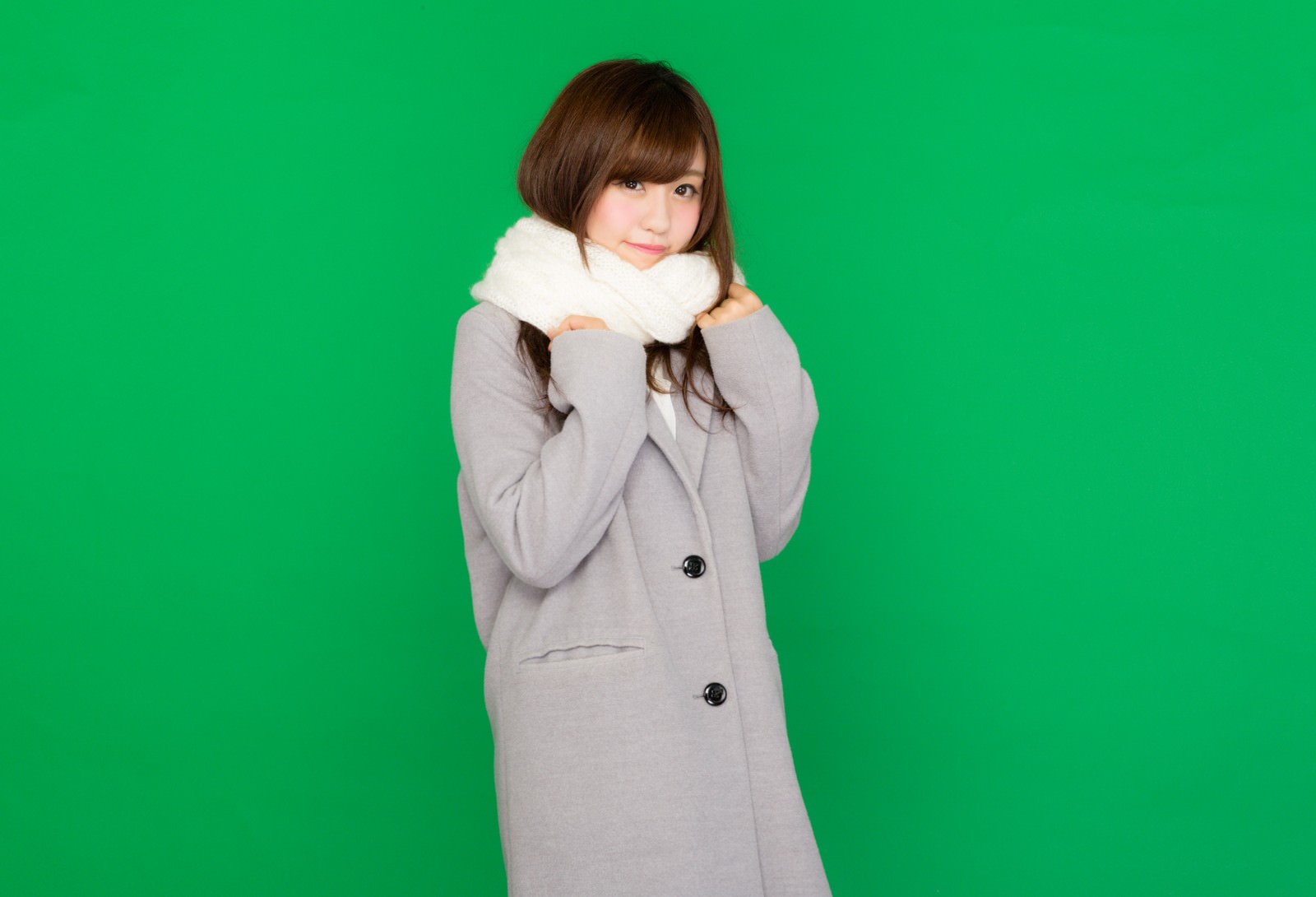 グレーコートに白いマフラーを巻いてグリーンバックの前に立つ女性［モデル：河村友歌］