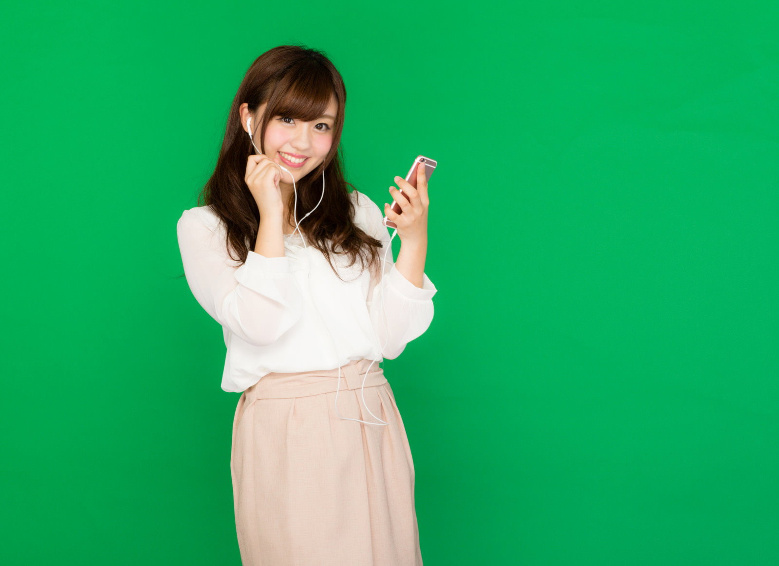 グリーンバックの前でイヤホンマイクをつけスマホで通話する女性［モデル：河村友歌］