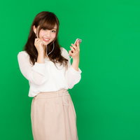 イヤホンマイクで通話する女性（グリーンバック背景）の写真