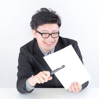 ノートとペンを持って笑顔で下を向くスーツの男性の写真