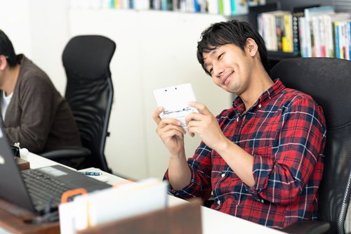 携帯ゲーム機を持って本棚の前に座る男性