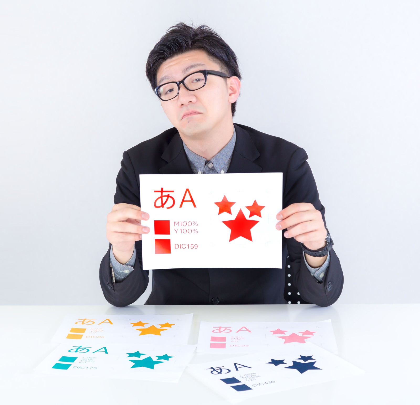 カラーバリエーション見本を両手で持つスーツ姿の眼鏡男性デザイナー［モデル：OZPA］