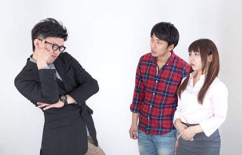 白い紙を持つスーツの男性を囲む3人のオフィス風景