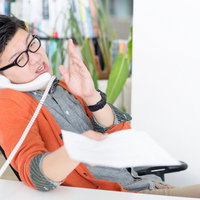 電話しながら書類を持つオレンジシャツの男性の写真