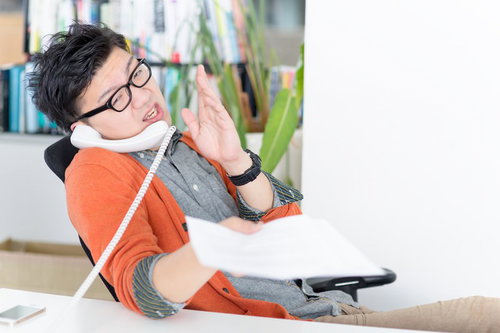 電話しながら書類を持つオレンジシャツの男性