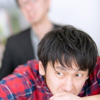 両手を組んでテーブルに置き前を見つめる男性の写真