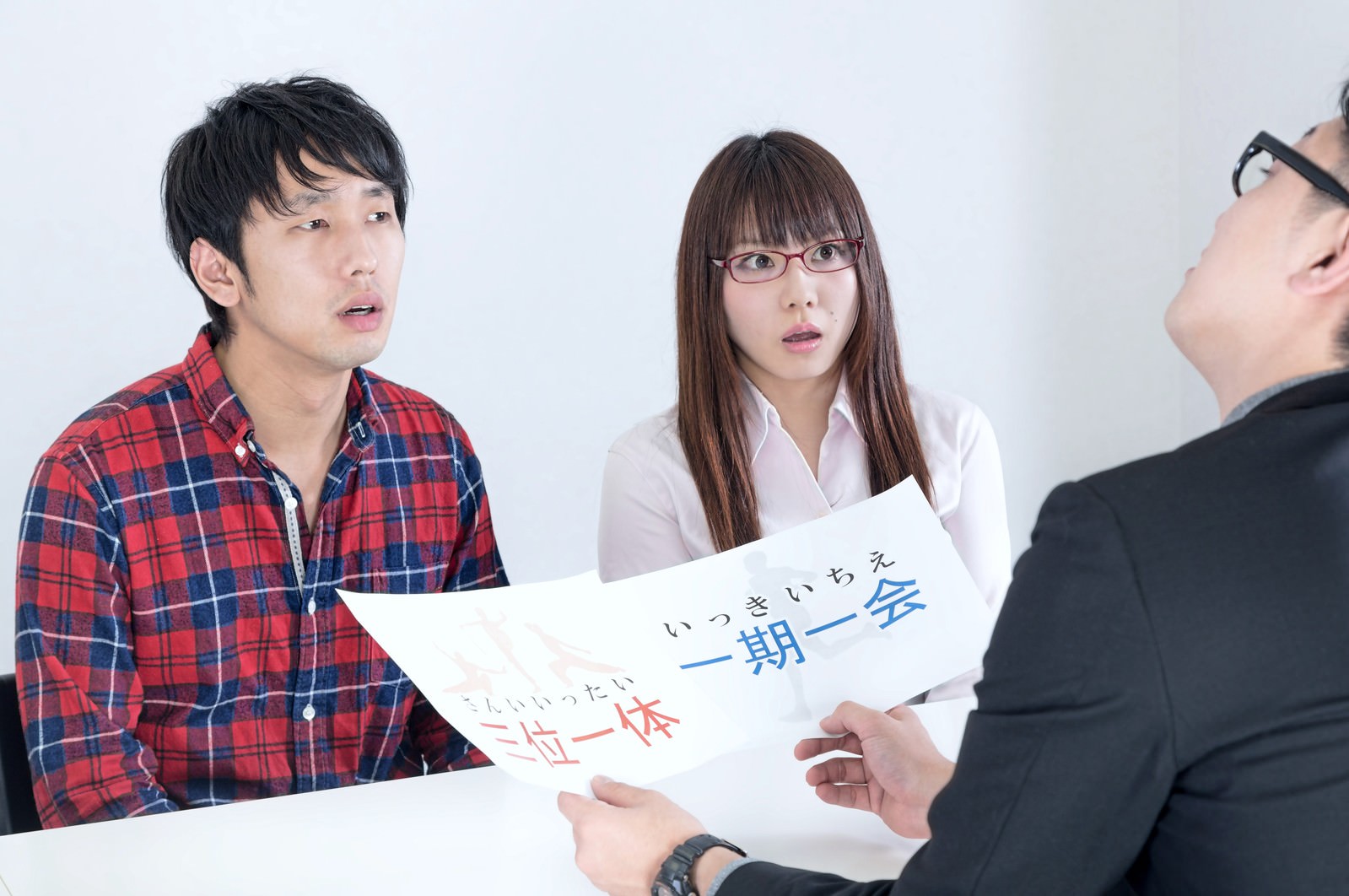 資料を見ながら対面する赤チェック柄シャツの男性と眼鏡の女性、紺ジャケットの男性の3人［モデル：大川竜弥 Lala OZPA］
