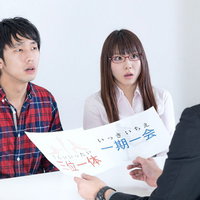 「一期一会」の紙を見る3人のオフィス風景の写真