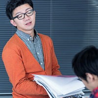 白い書類の束を両手で持つ眼鏡の男性の写真