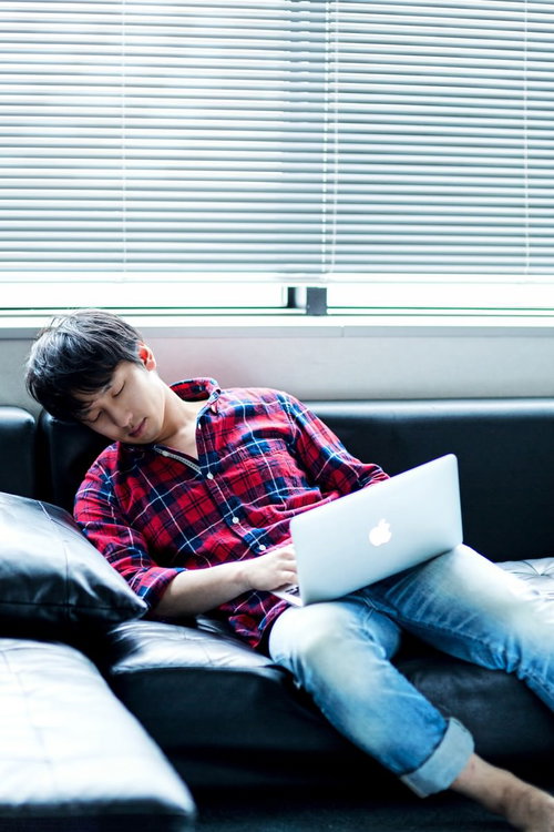 ソファでノートパソコンを操作するチェックシャツの男性