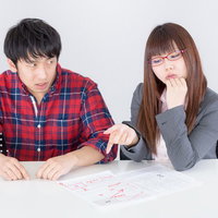 テーブルで赤い文字の書類を見る男性と女性の写真