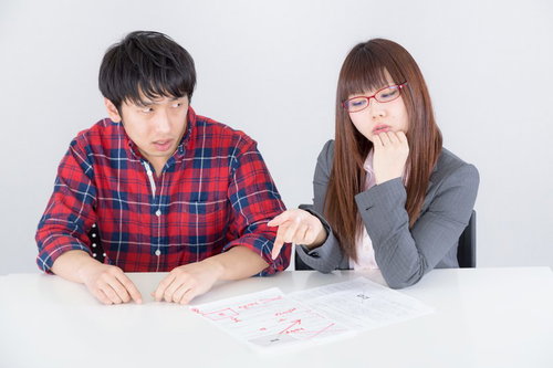 テーブルで赤い文字の書類を見る男性と女性