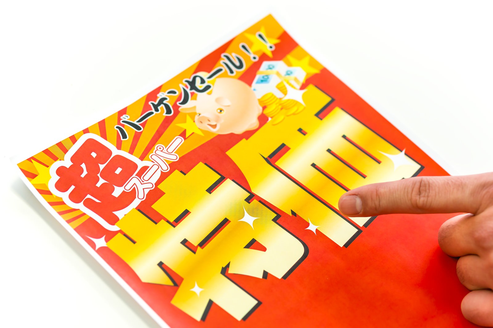 赤と黄色の背景に黄色いテキストと赤いロゴが配置された、子どもキャラクター入りのカルタ札に手指が触れている