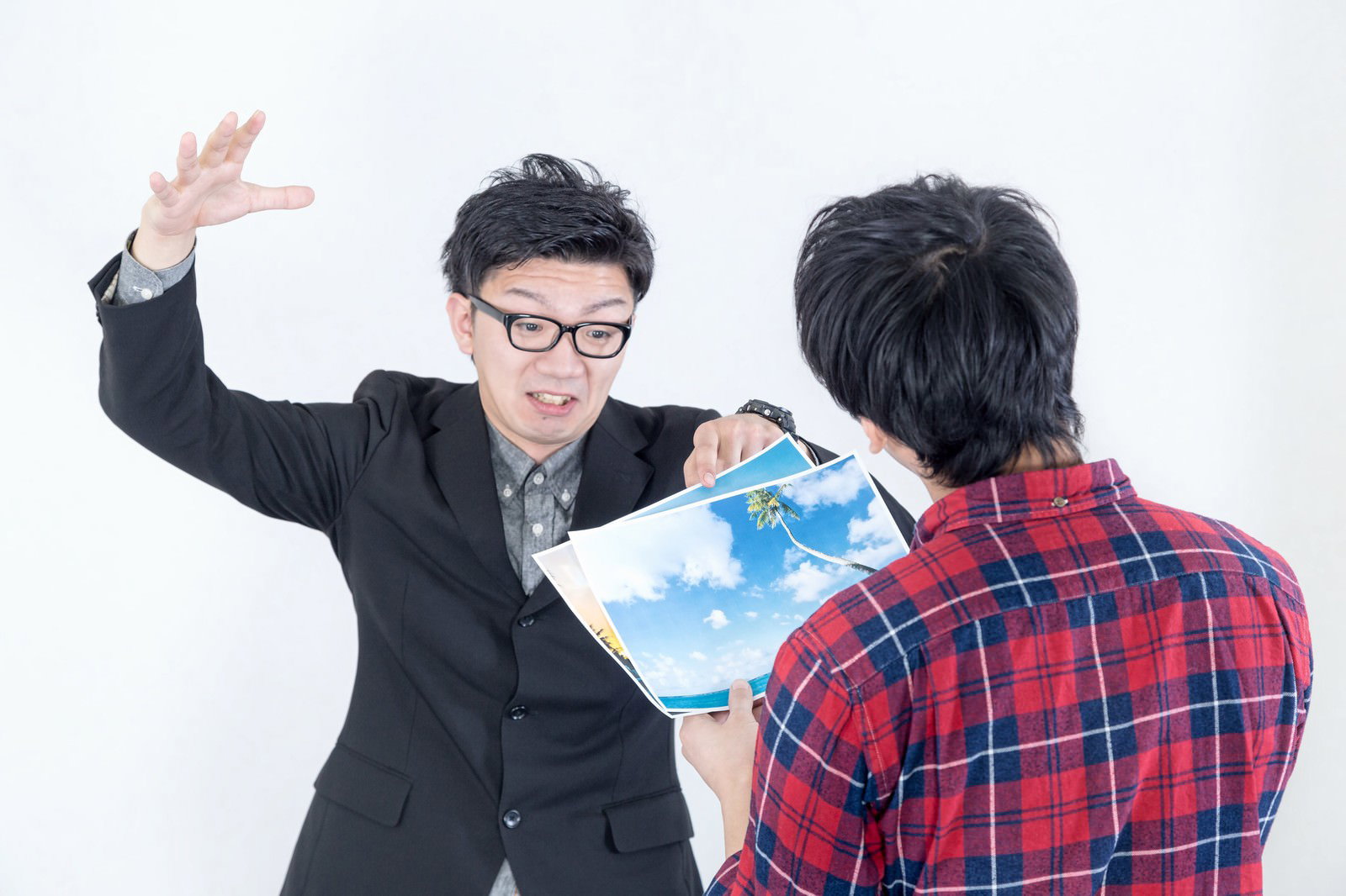 ハワイの写真を持ち説得するスーツ姿の男性と、それを聞くチェック柄シャツの男性［モデル：大川竜弥 OZPA］