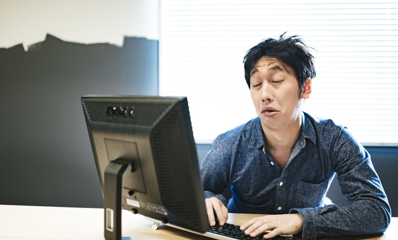 オフィスのデスクに座り、パソコンの前で頬杖をついて疲れた表情で画面を見つめる男性［モデル：大川竜弥］