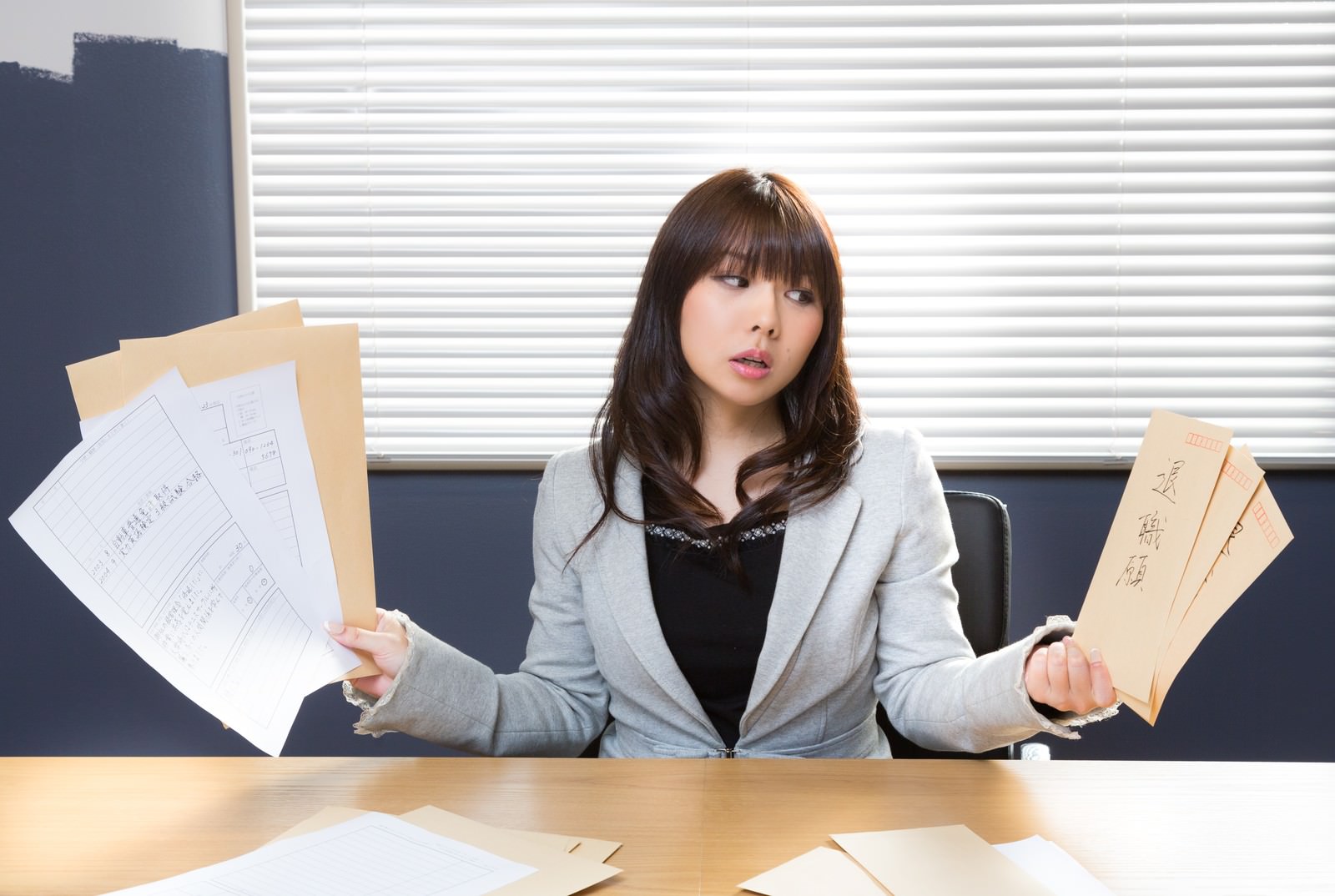 退職願と引き継ぎ書類を持つ困惑した女性社員［モデル：Lala］