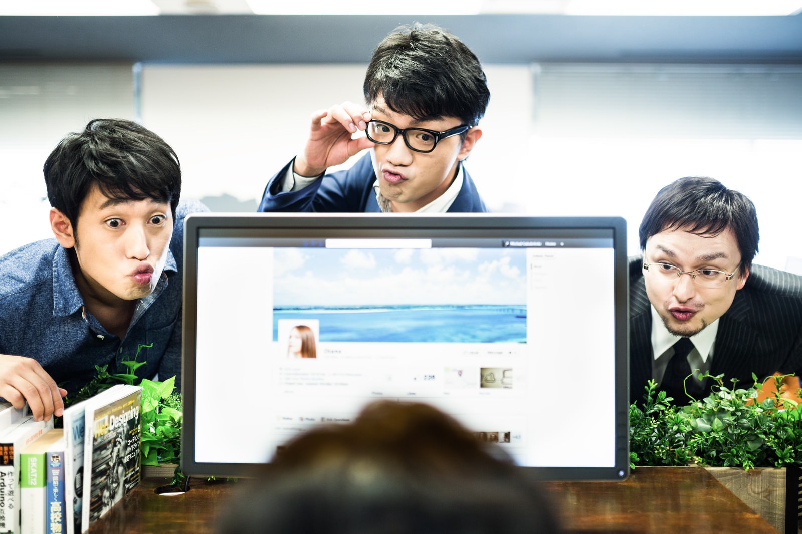 職場のパソコン前で3人の男性社員。手前の男性が困惑し、奥の先輩が眼鏡を持ち上げてひやかしている［モデル：大川竜弥 OZPA Max_Ezaki］