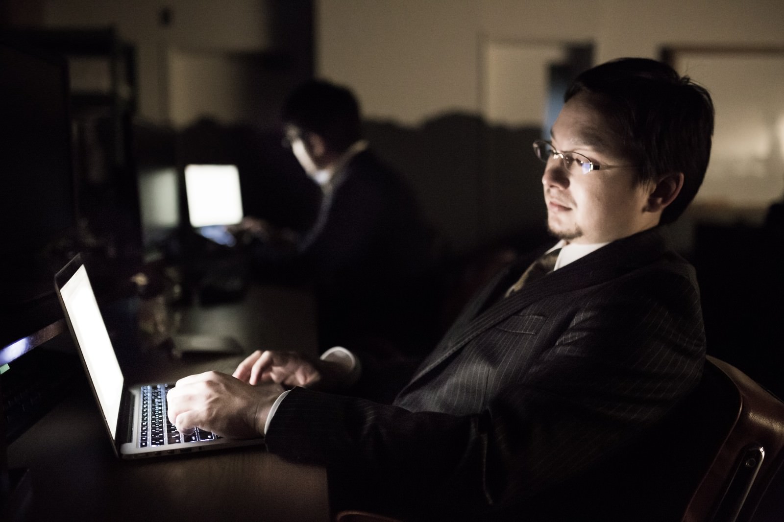 薄暗いオフィスで深夜にPCを操作する男性［モデル：Max_Ezaki］