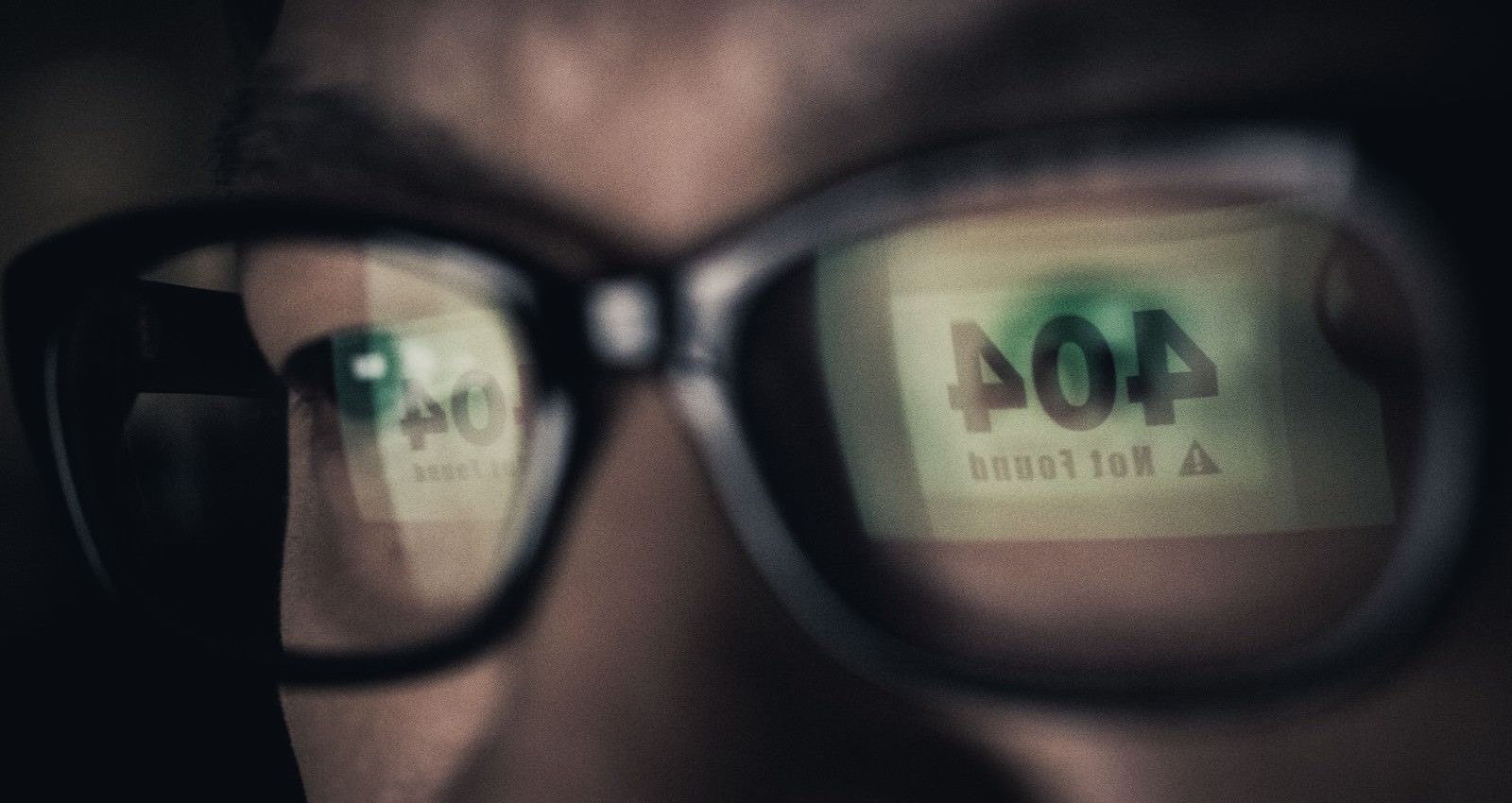 暗い部屋で眼鏡のレンズに404 Not Foundの文字が反射して映っている人物のアップ［モデル：OZPA］
