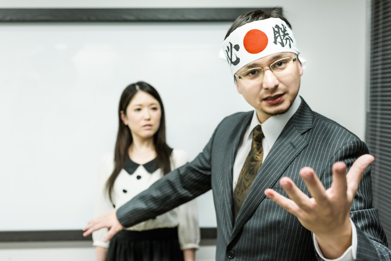 はちまきを巻いてスピーチするスーツ姿の男性［モデル：Max_Ezaki シマヅ］