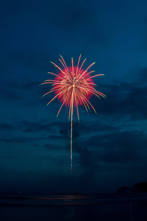 海上から打ち上がる赤とピンクの花火の光跡