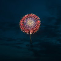 日が落ちてきた夜空に上がる赤と白の打上花火の写真