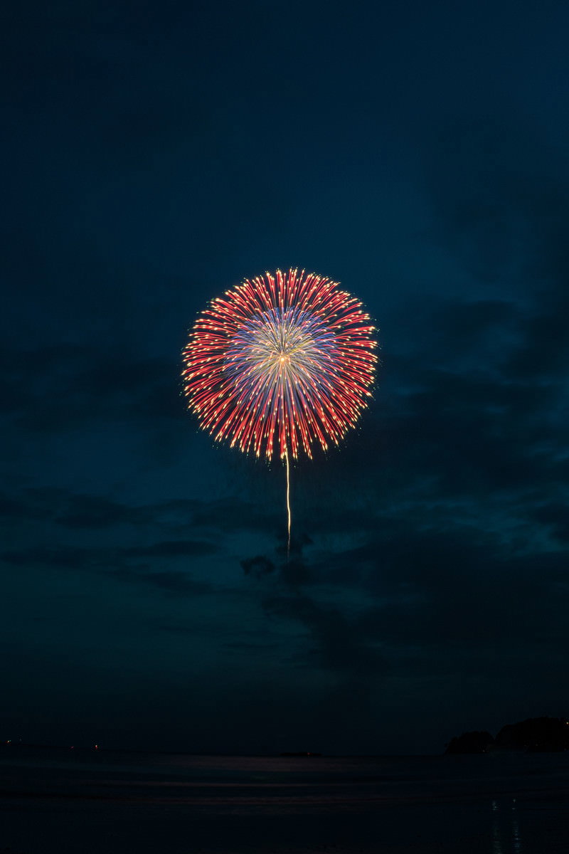 暗い夜空に赤と白の光が放射状に広がる打ち上げ花火