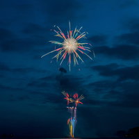 花火大会を砂浜から撮影した夜空と海上花火の写真