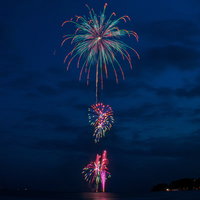 夜空に開く打上花火と水面への光の映り込みの写真