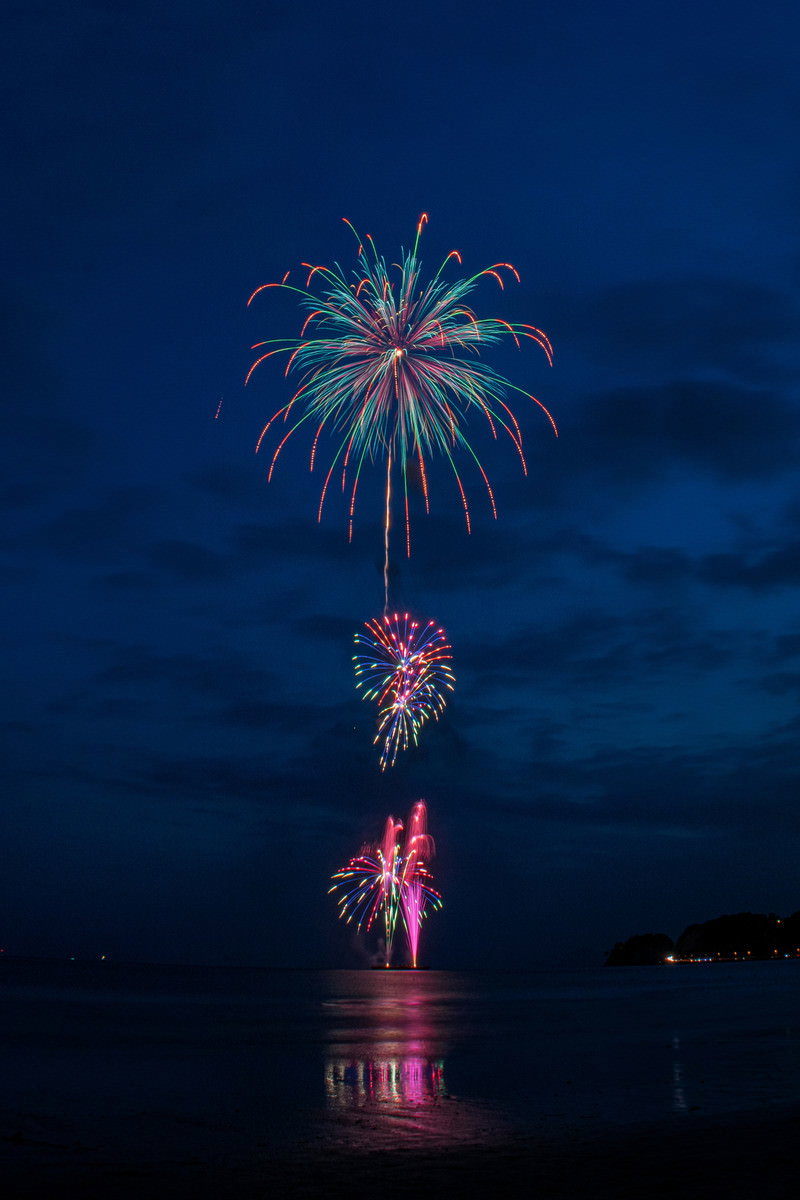 夜空に色とりどりの花火が開き、水面に光が映り込む様子