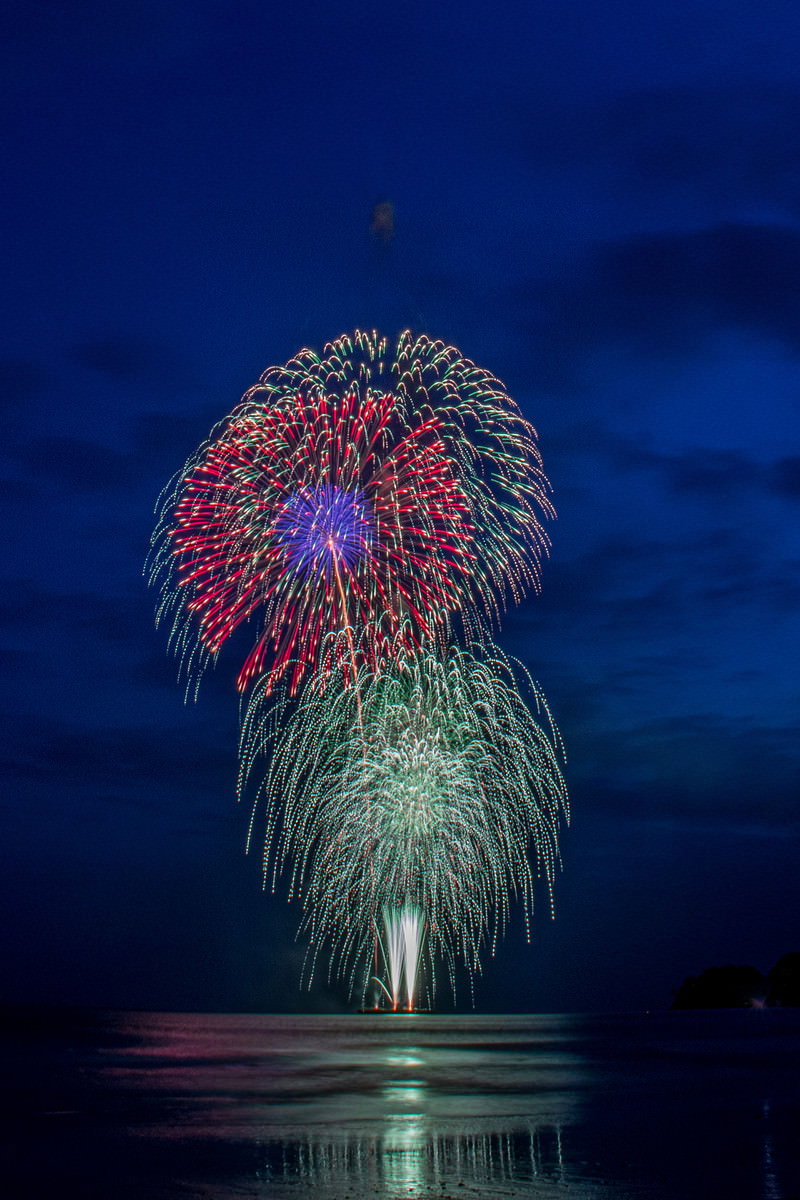 夜空に打ち上げられた色とりどりのスターマイン花火と海面への反射
