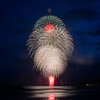 海上に打ち上がる大輪の白い打上花火が水面に映る夜景の写真