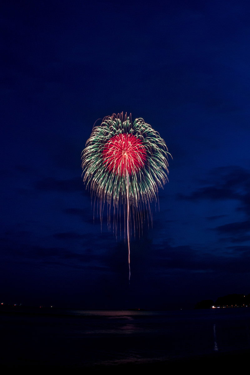 深い夜空に赤と金色の打上花火が大きく開いている様子