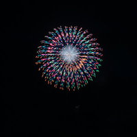 夜空に大きく開く玉虫色の打上花火が放つ色とりどりの光の写真