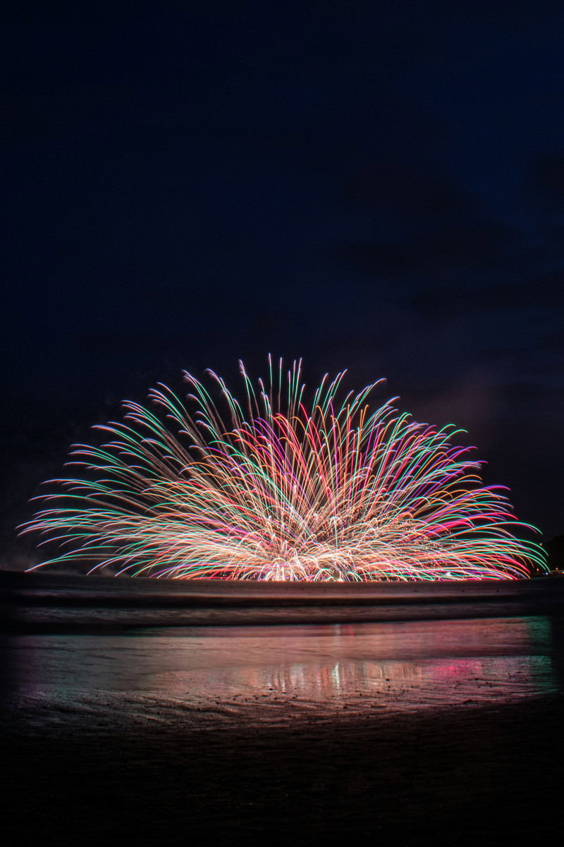 夜空に連発で打ち上がる水中花火と海面への光の反射